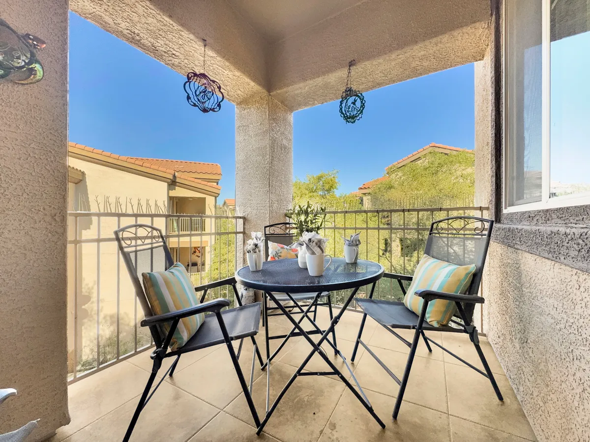 A cozy round table with four chairs sits on a patio surrounded by flowers and decorative hanging ornaments. The space is ideal for al fresco dining, morning coffee, or quiet conversations, with a relaxed, welcoming feel.