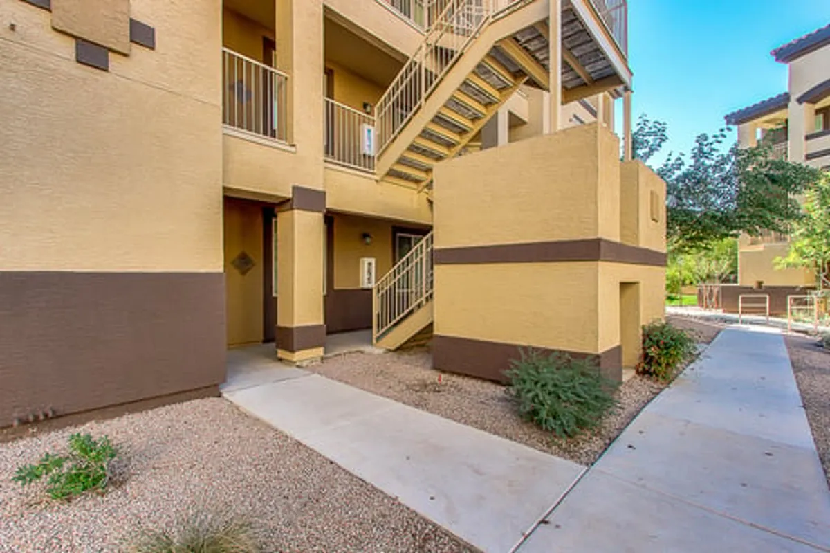 An exterior shot highlighting the staircase and building facade, with a clear pathway leading up. The upstairs location is suggested, and the scene has a welcoming, community-oriented mood.