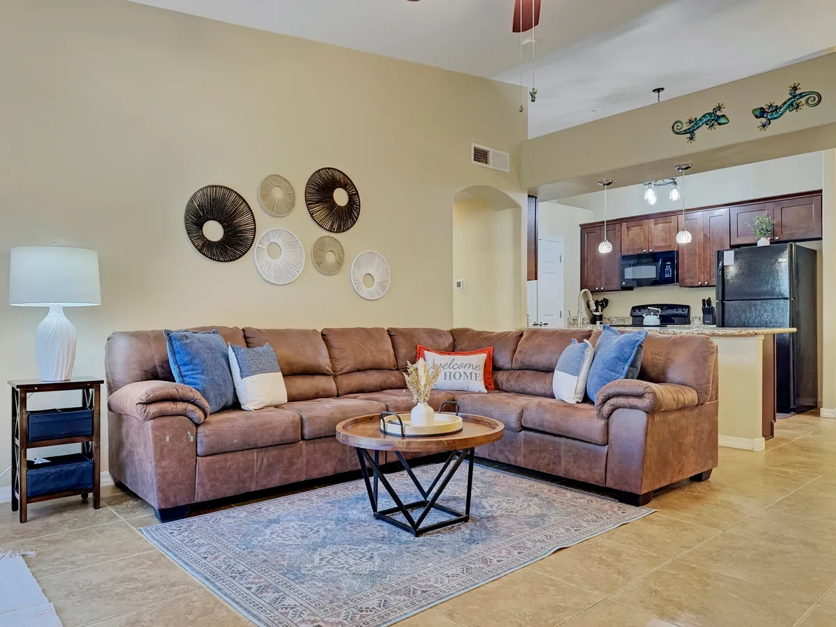 A cozy interior featuring a brown sectional sofa with decorative pillows, a coffee table with décor, and wall art. The scene illustrates a comfortable space ideal for informal gatherings, morning coffee, or unwinding after a productive day.