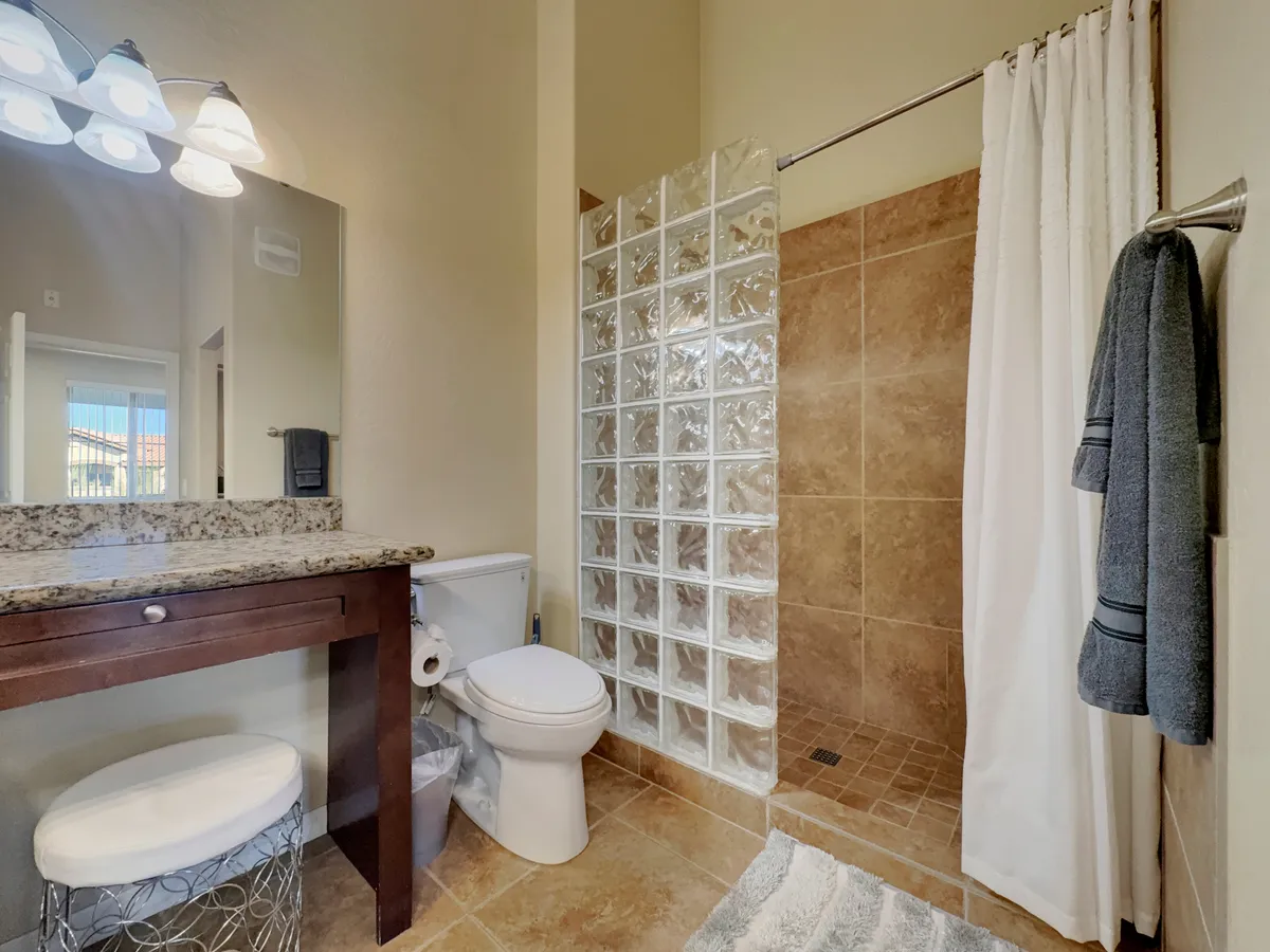 A modern bathroom featuring a granite countertop with a vanity mirror, a glass block shower, and a neatly arranged towel rack. The space exudes serenity and fresh cleanliness, perfect for unwinding after a long day or starting the morning refreshed.