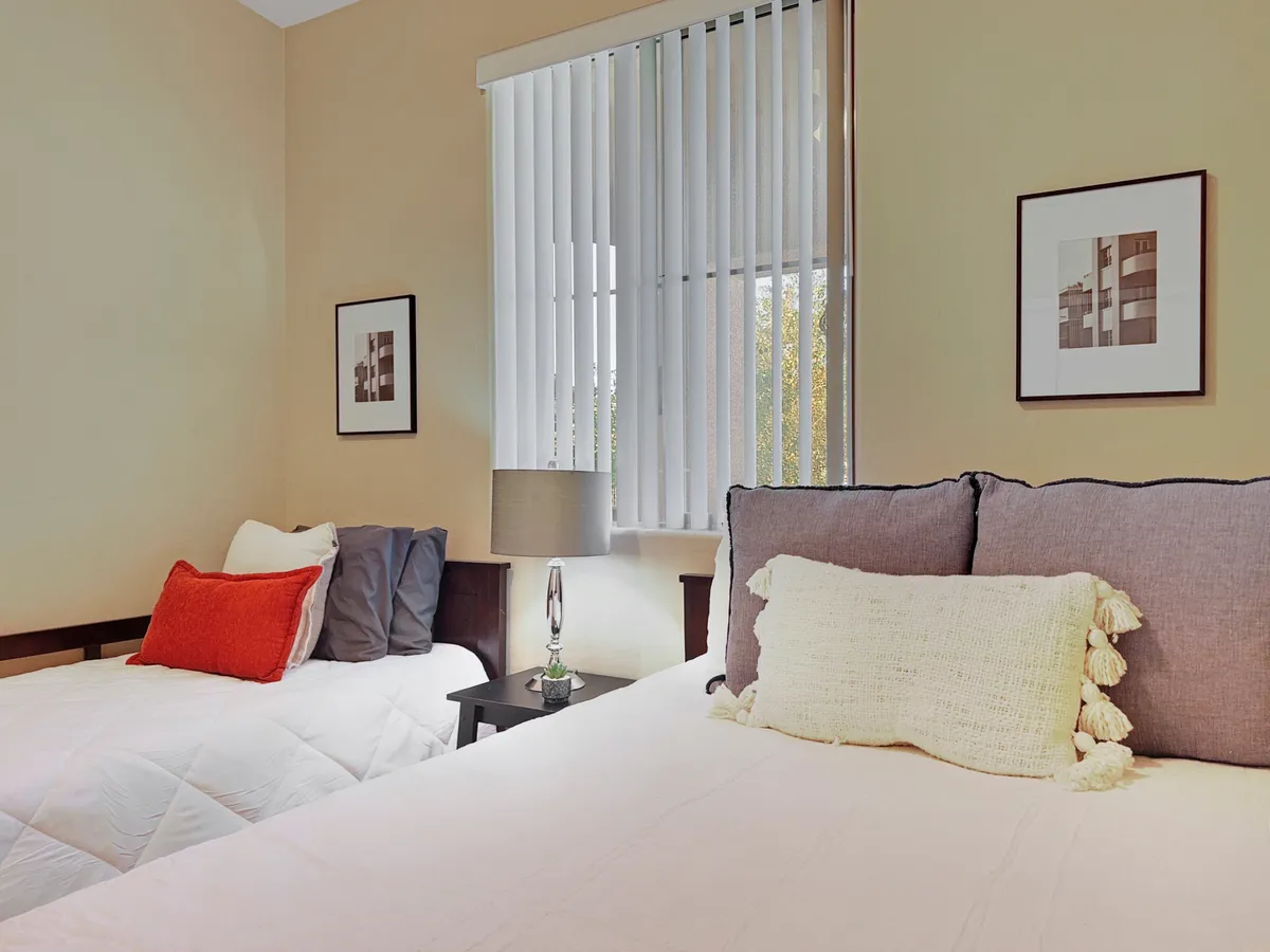 A guest bedroom with two beds adorned with decorative pillows, a nightstand with a warm lamp between them, and framed artwork on the wall. The inviting space is designed for flexibility, perfect for families or groups seeking comfort and versatility.