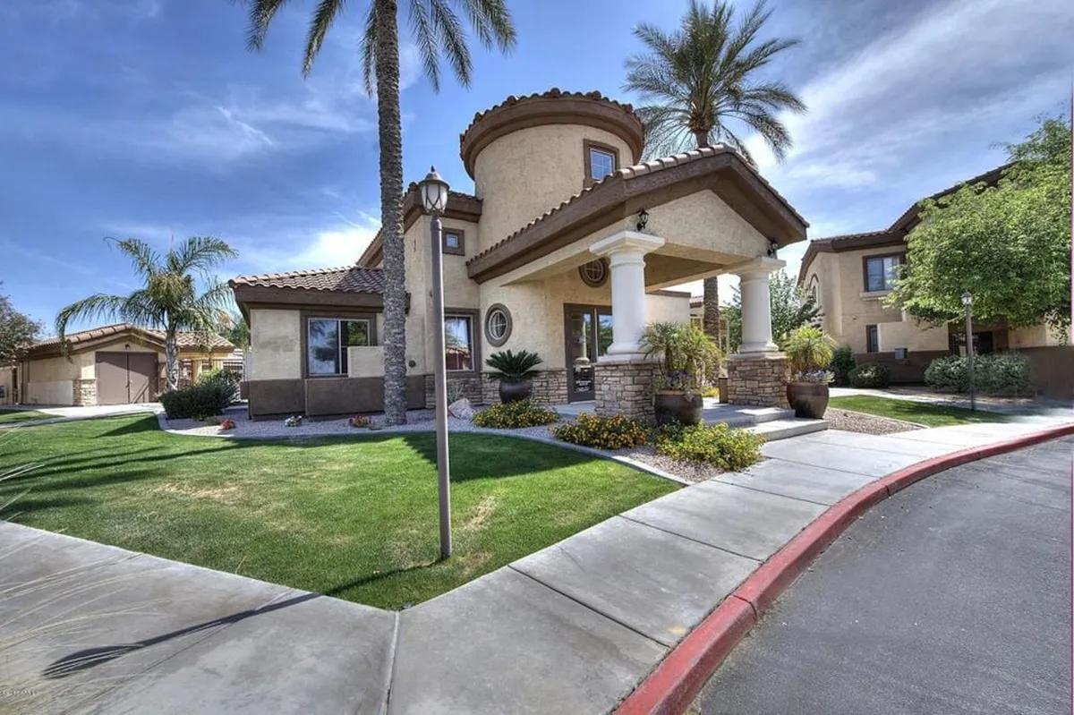 An inviting exterior view featuring palm trees, a landscaped garden, and the architectural features of the house. The scene evokes a sense of tranquility, with a porch area that suggests relaxation and social gatherings amidst natural beauty.